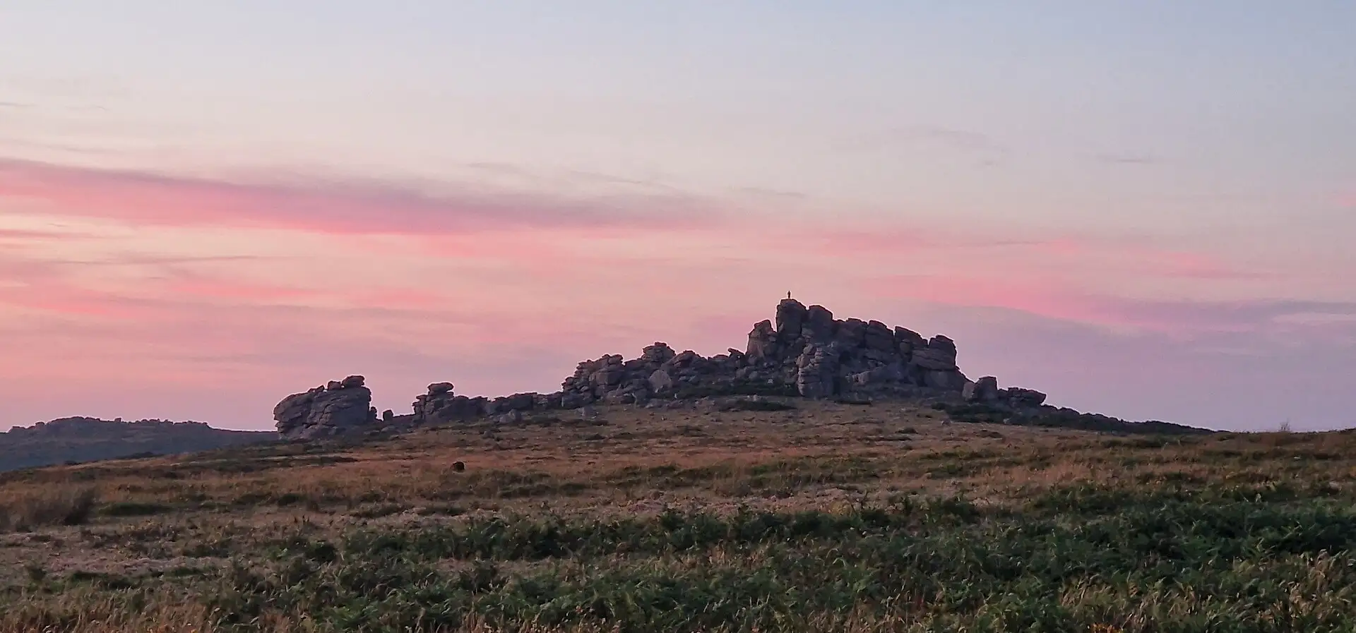 Hound Tor's granite stacks silhouetted against a pink sunset sky